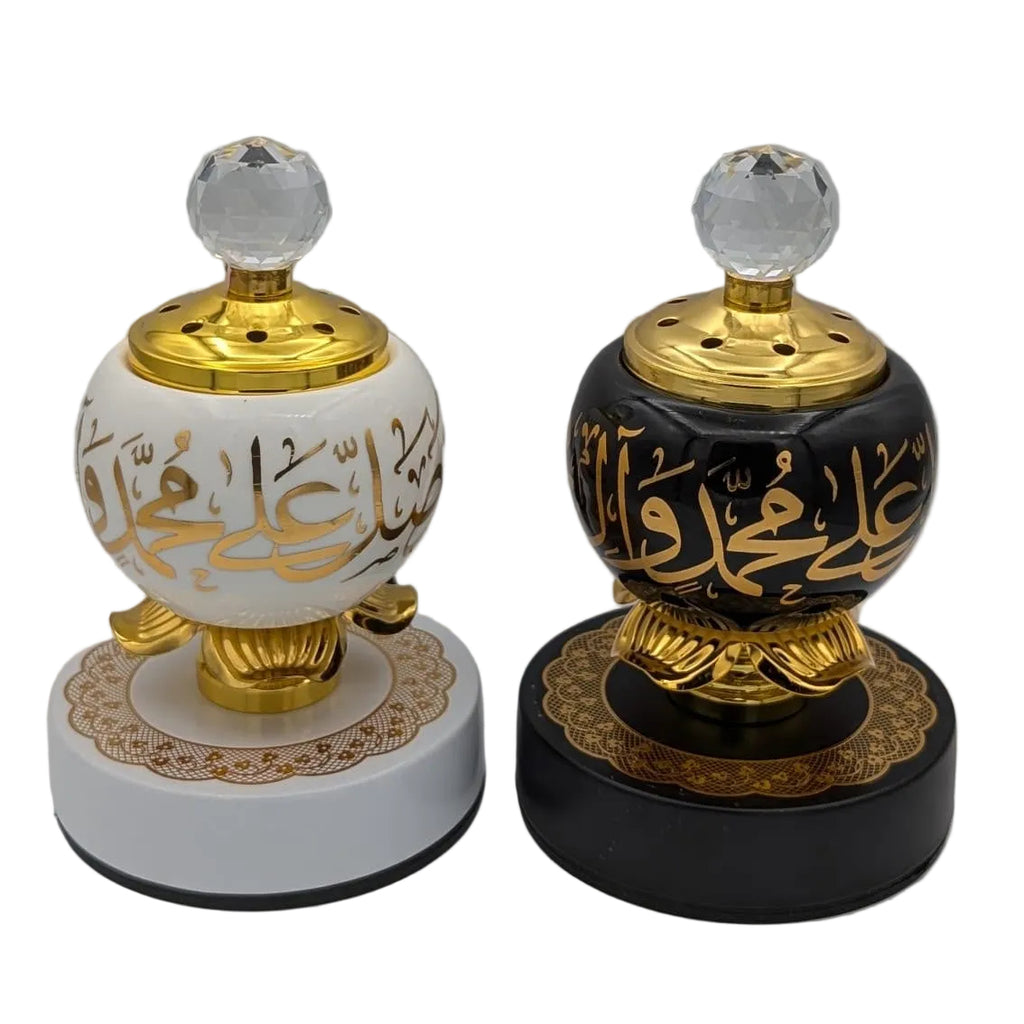 Two decorative incense burners with Arabic calligraphy, one white and one black, both featuring gold accents and clear crystal tops, displayed on a neutral gray background.